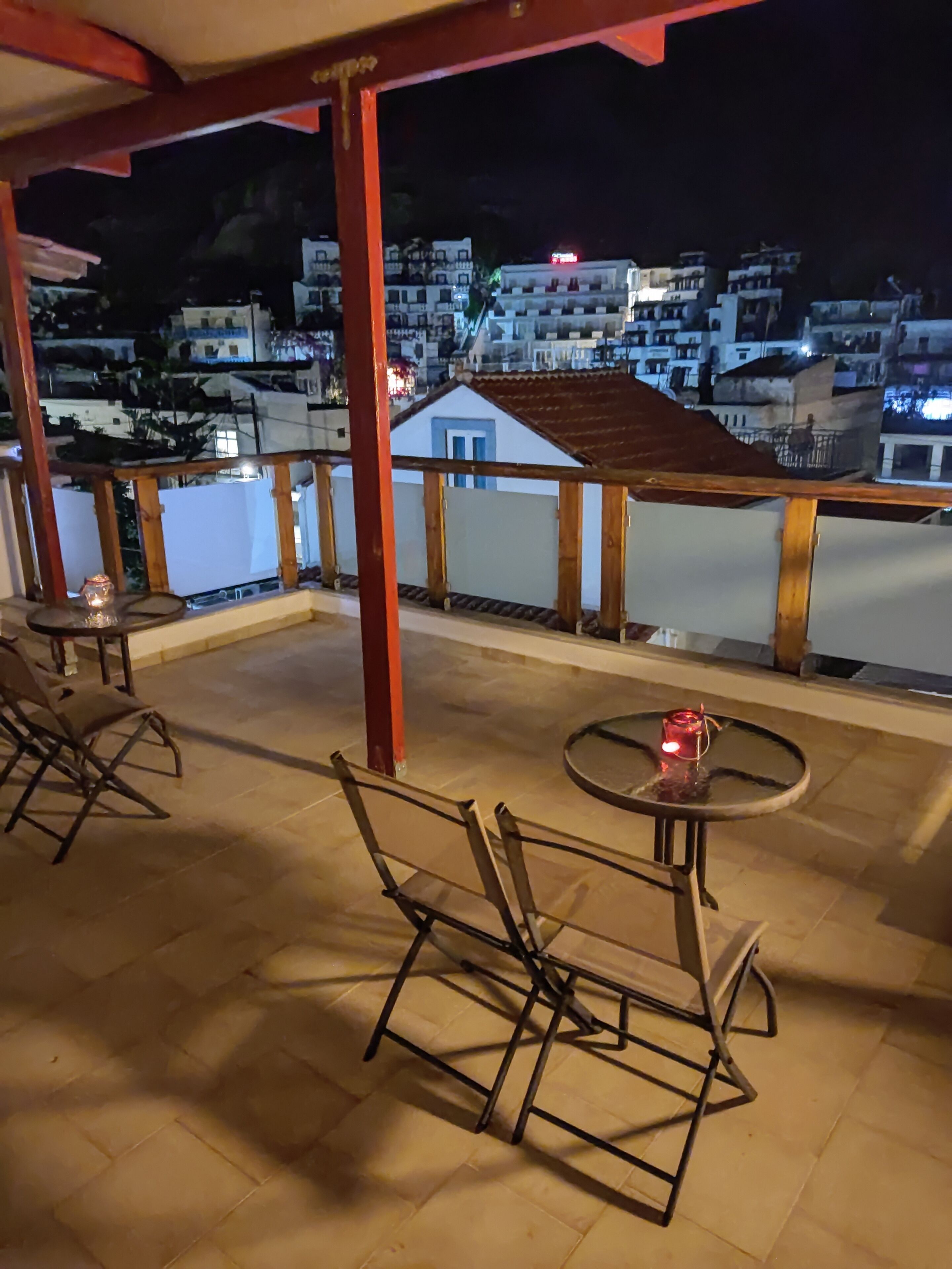 Un balcón con sillas y una mesa, con vista a una zona residencial de noche.