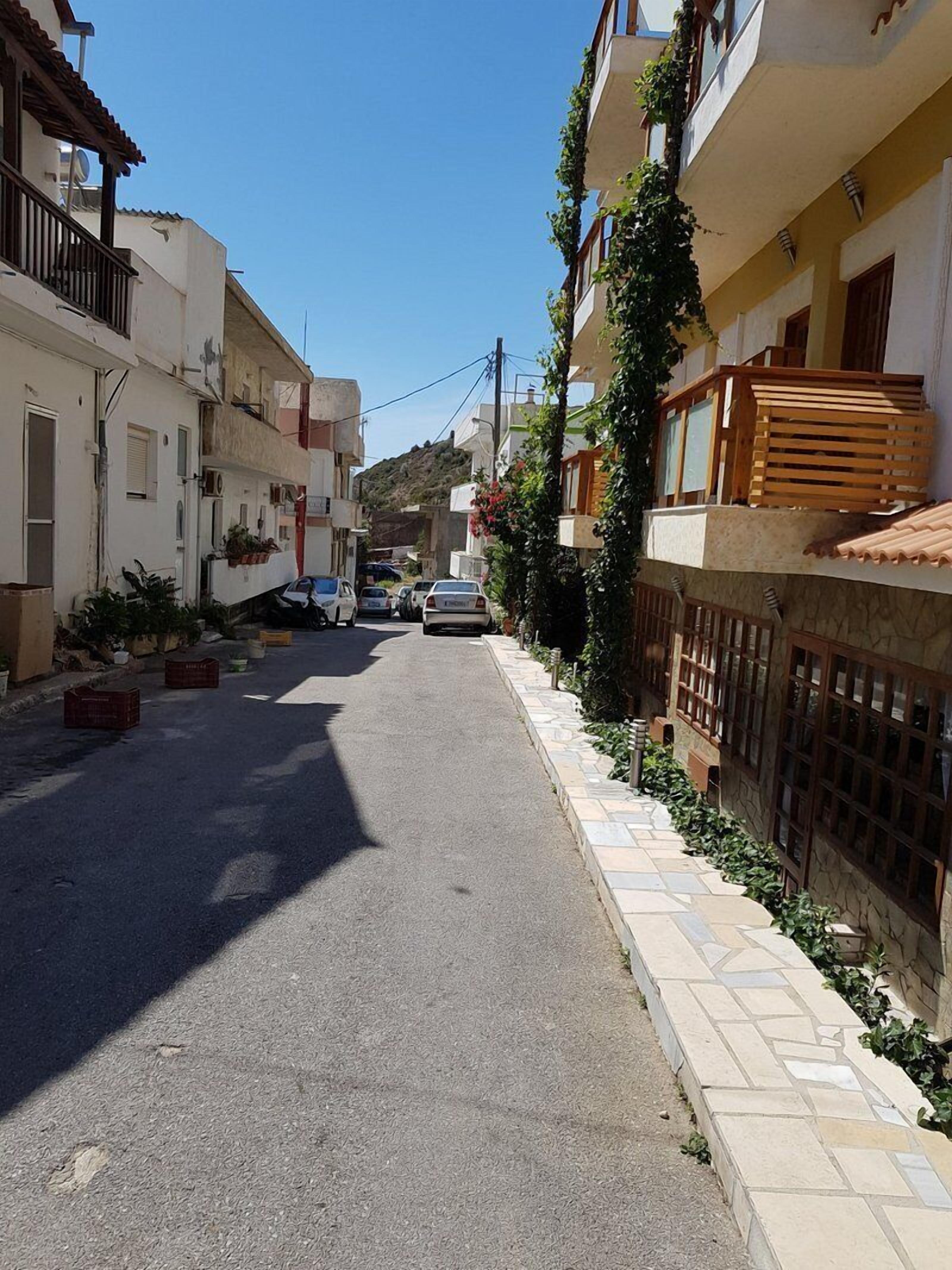 Une rue étroite bordée d’immeubles à plusieurs étages, dont certains sont dotés de balcons et de plantes.