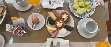 Una mesa de desayuno con platos de comida, incluyendo tostadas, huevos y fruta, además de un vaso de zumo de naranja.