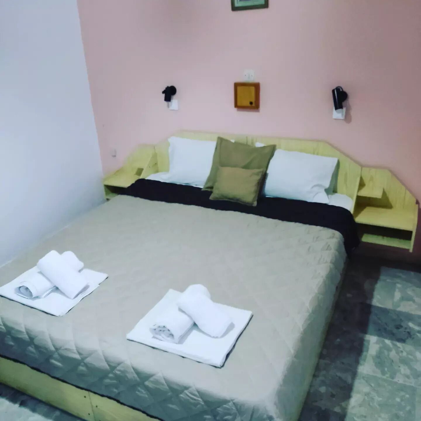 A neatly made bed with a beige bedspread, two pillows, and rolled white towels on the bed.