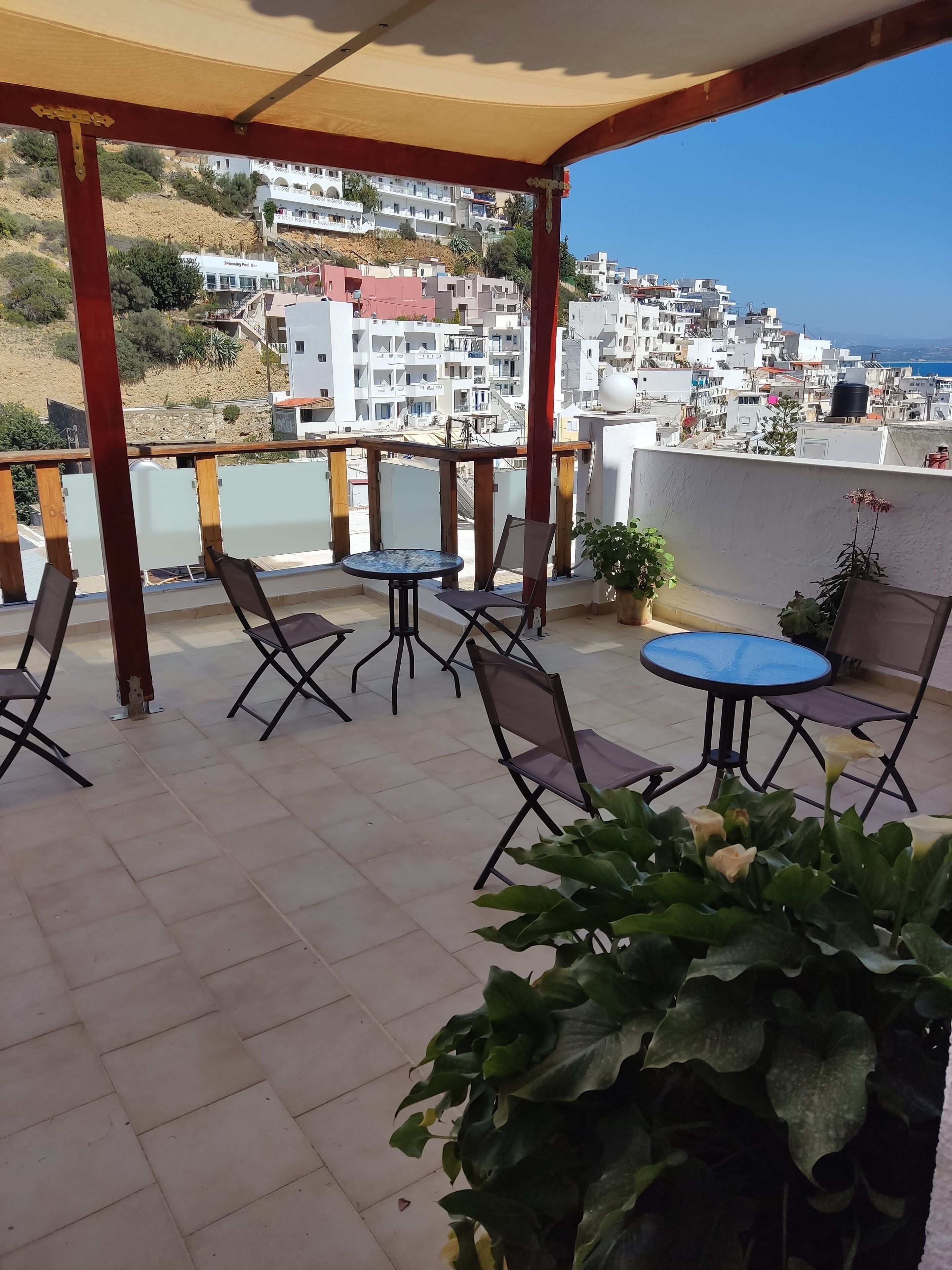 Una terraza con mesas y sillas, una planta en maceta y vistas a un pueblo en la colina.