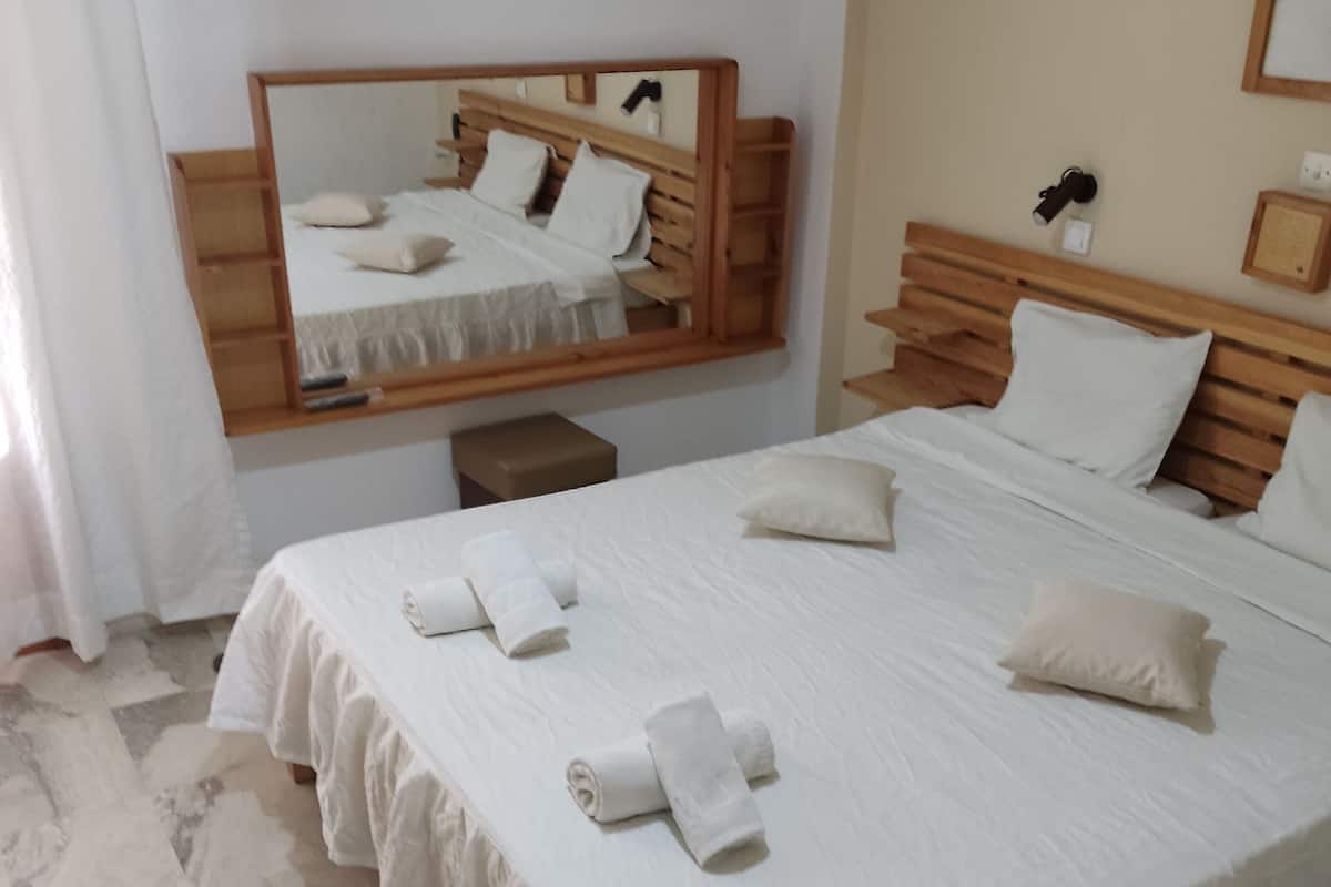 Una habitación de hotel con una cama grande, cabecera de madera, una mesita de noche y un espejo.