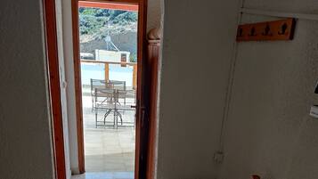 Una habitación con cama, una silla, una mesita y un refrigerador. Hay una puerta que da a un espacio exterior con una mesa y sillas.