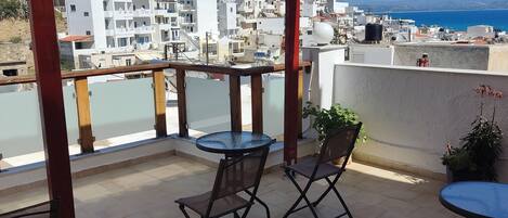Una terraza techada con dos mesas y sillas, con vistas a un pueblo costero y al mar.