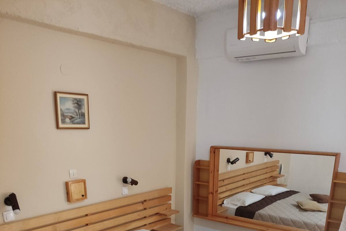 Un dormitorio con cama de madera, una mesita de noche, un espejo en la pared y un aplique de techo.