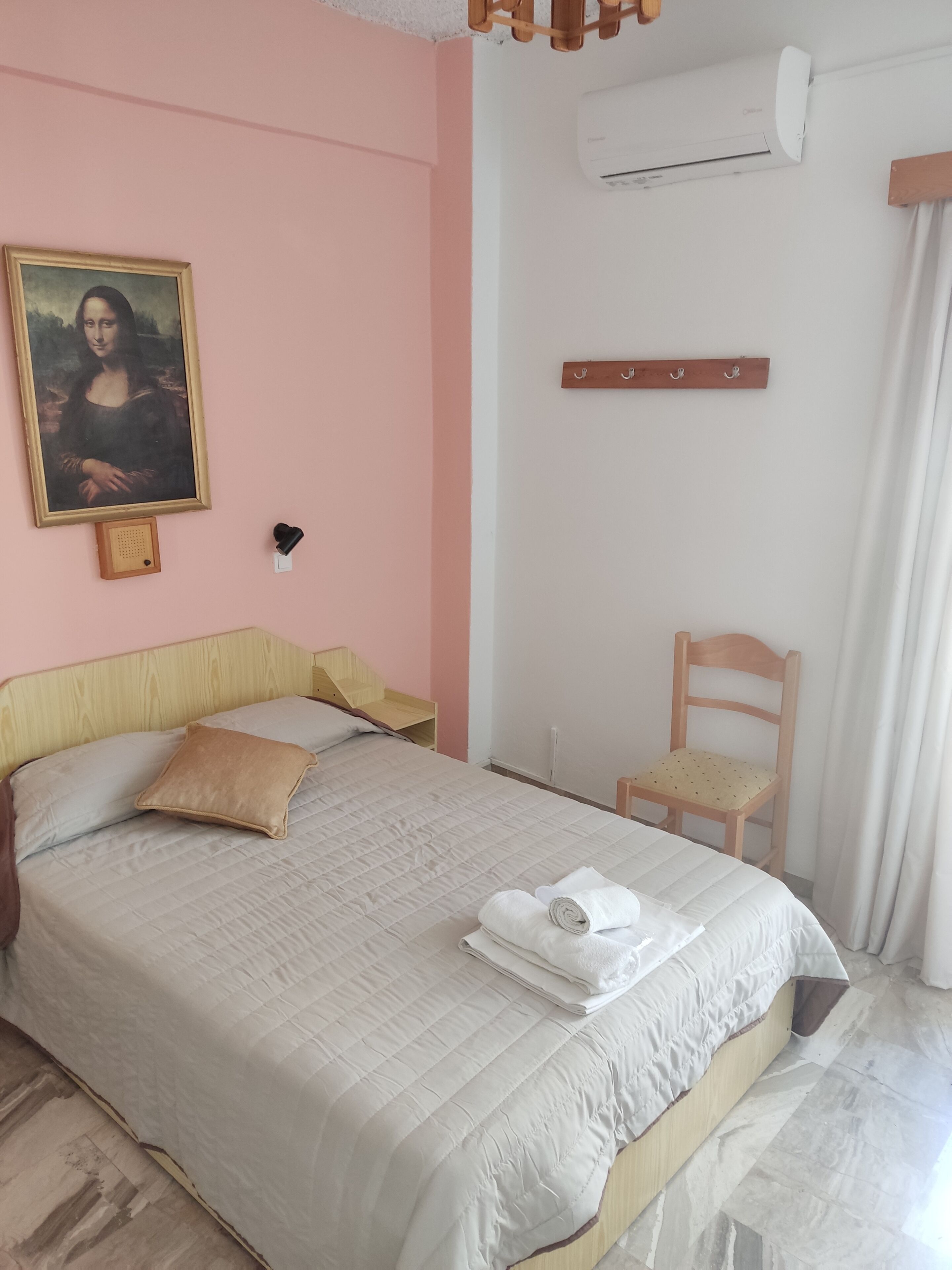 Ein ordentlich bezogenes Bett mit weißer, gesteppter Bettdecke, einem Holz-Kopfteil und einem Gemälde der Mona Lisa an der Wand.