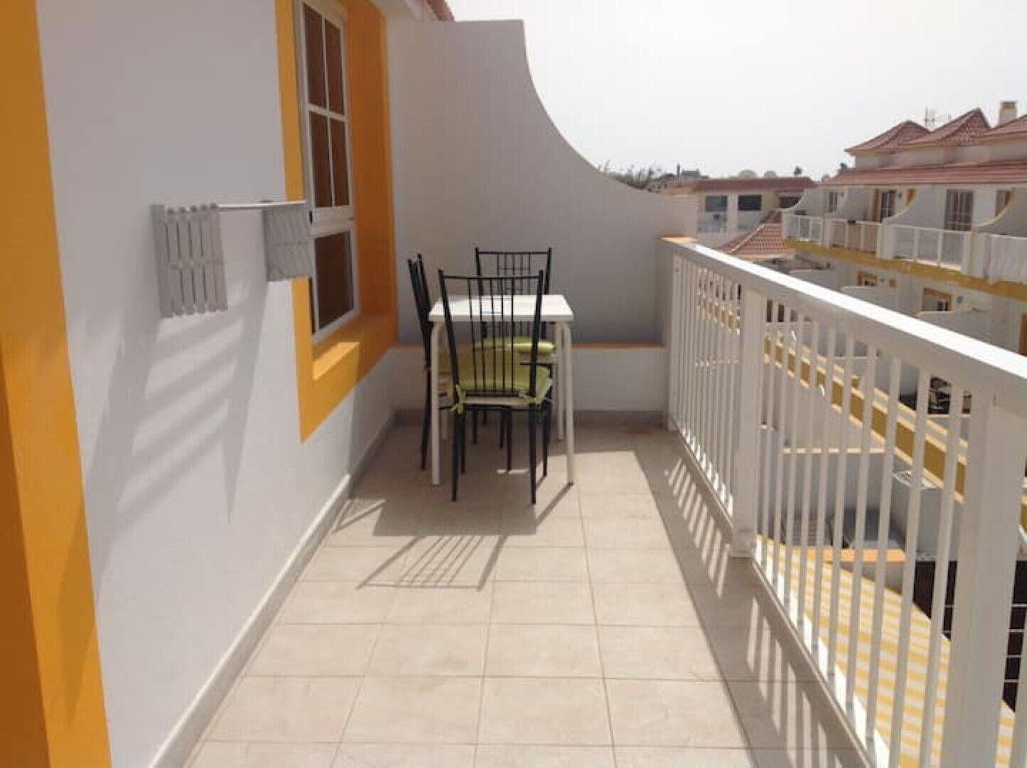 Un balcon avec une table et des chaises, une fenêtre et une rambarde blanche.