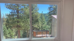 A dining area with a round table and four chairs, a window with a view of a forest and a deck, and a can on the table. - Unique Property in the Southern Utah Mountains near Duck Creek Village  (Duck Creek Village)