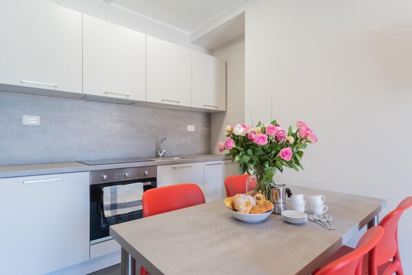 A modern kitchen with white cabinets, a stainless steel sink, and a dining table set with a bowl of pastries, a coffee pot, and white cups.