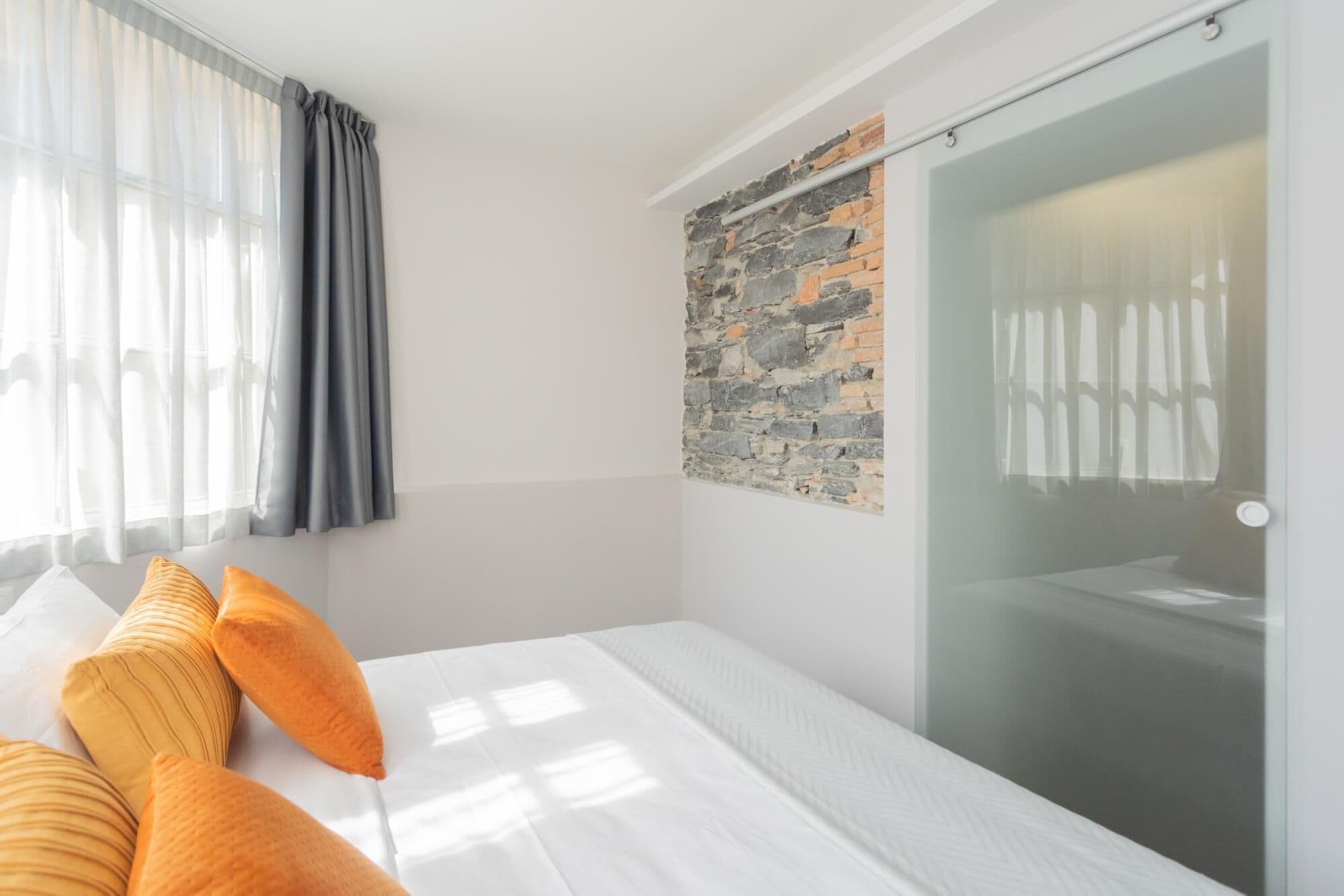 Ein Hotelzimmer mit Bett, Duschkabine aus Glas, Steinwand und transparenten Vorhängen.