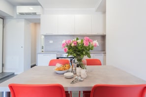 A modern kitchen with white cabinets, a dining table with red chairs, and a vase with flowers.