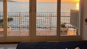 Una habitación con vista al atardecer sobre el mar, un balcón con sillas y una cama con toalla.