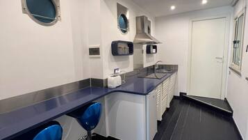 Una cocina moderna con encimera oscura, dos taburetes azules, horno empotrado y una puerta blanca.