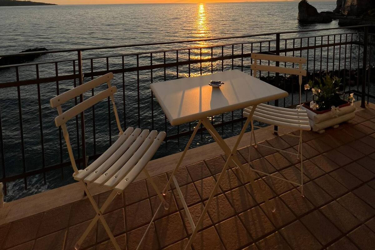 Een terras met een tafel en stoelen met uitzicht op zee bij zonsondergang.