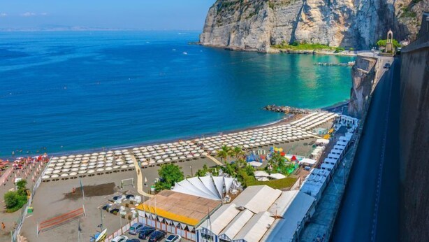 Un hotel frente al mar con zona de playa, acantilados y una vía de tren que corre paralela a la playa.