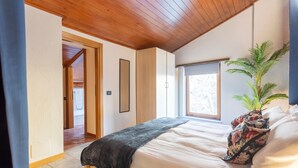 A bedroom with a wooden ceiling, a bed with a floral pillow, a window, and a plant. - San Fedele Apartments (Como)