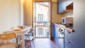 A compact kitchen with a dining area, a view through an open door, and a small balcony. - San Fedele Apartments (Como)