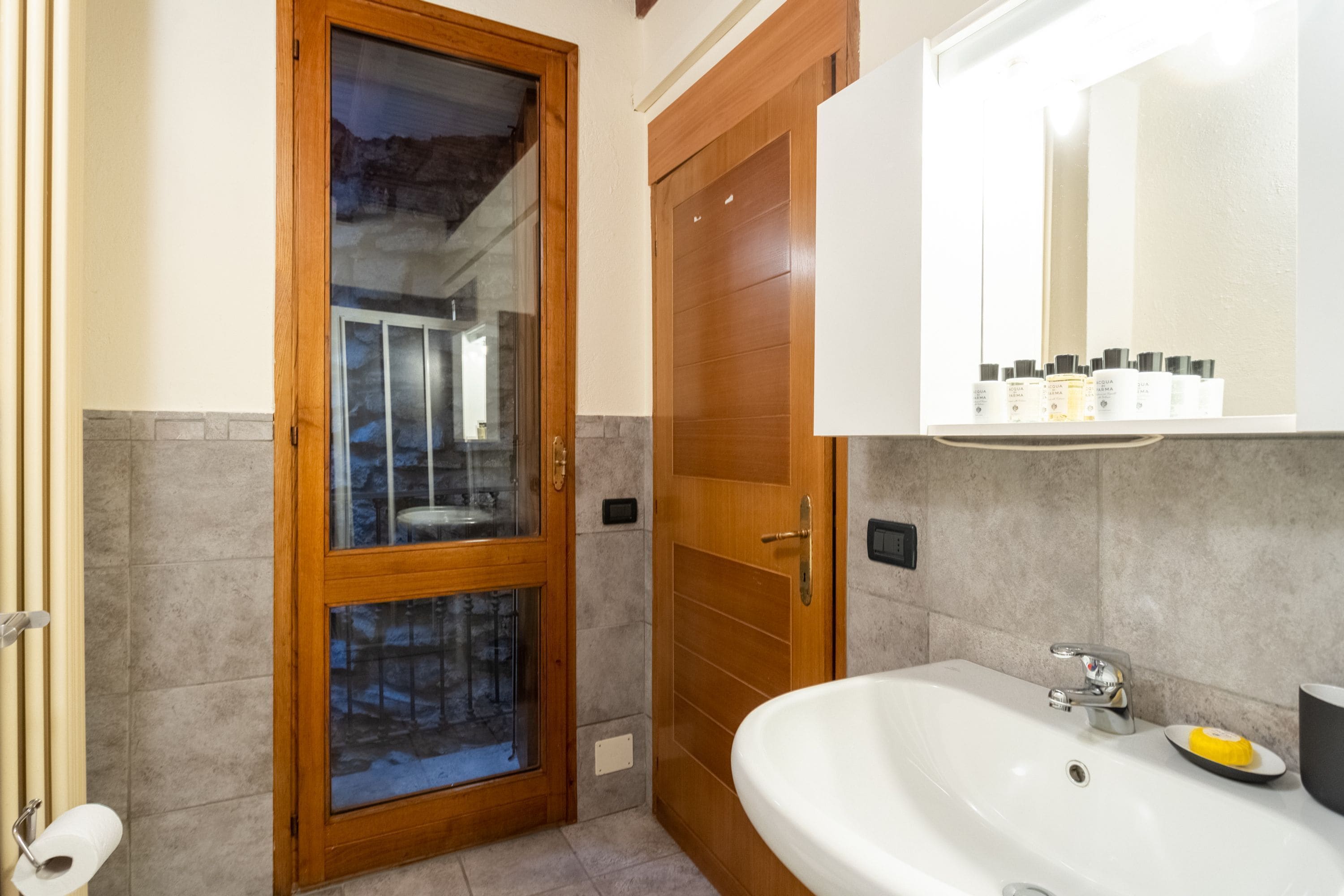 Une salle de bain avec une porte en bois, un lavabo blanc et un miroir au-dessus.