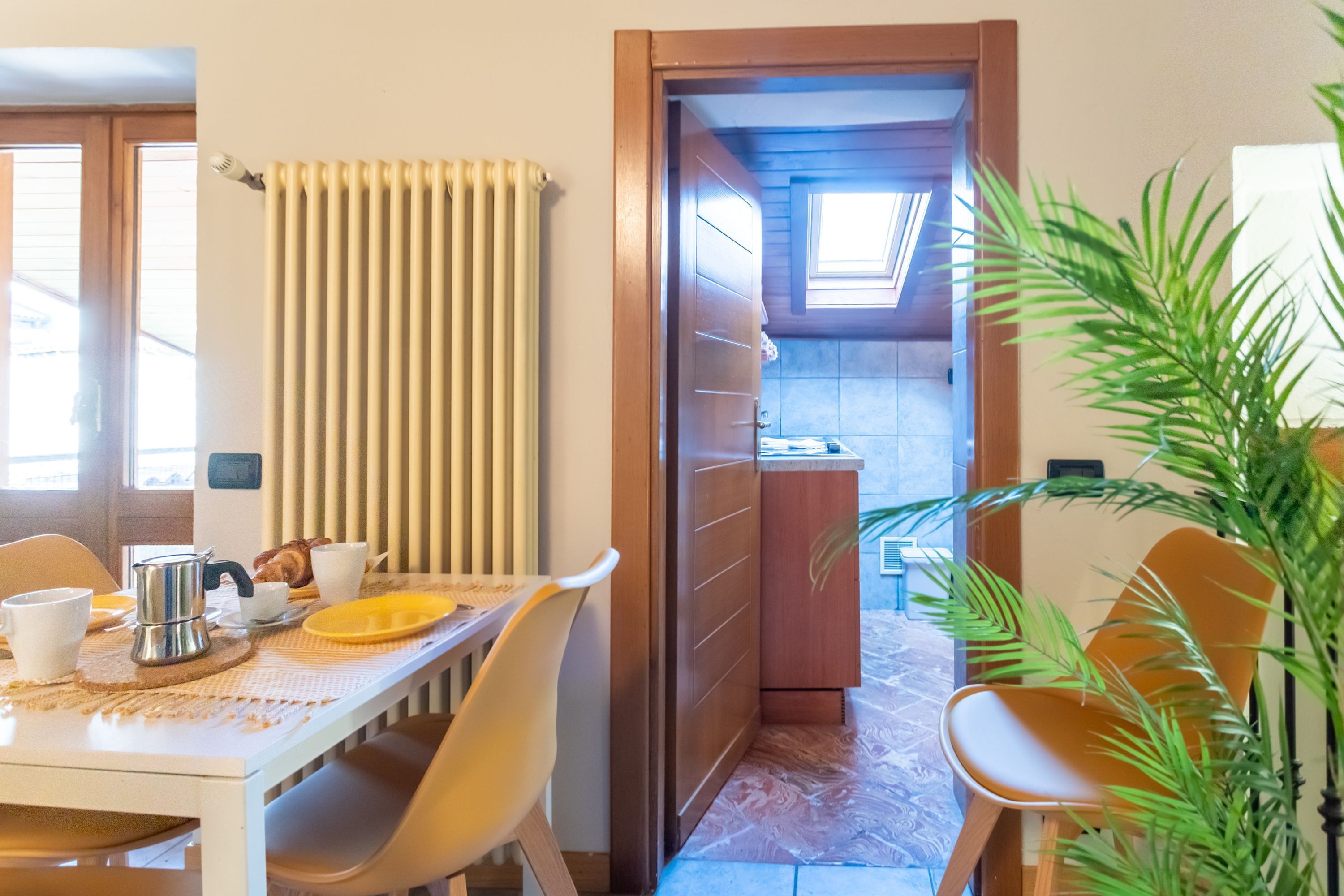 A dining area with a table set for two, a radiator, and a view into the kitchen through an open door.