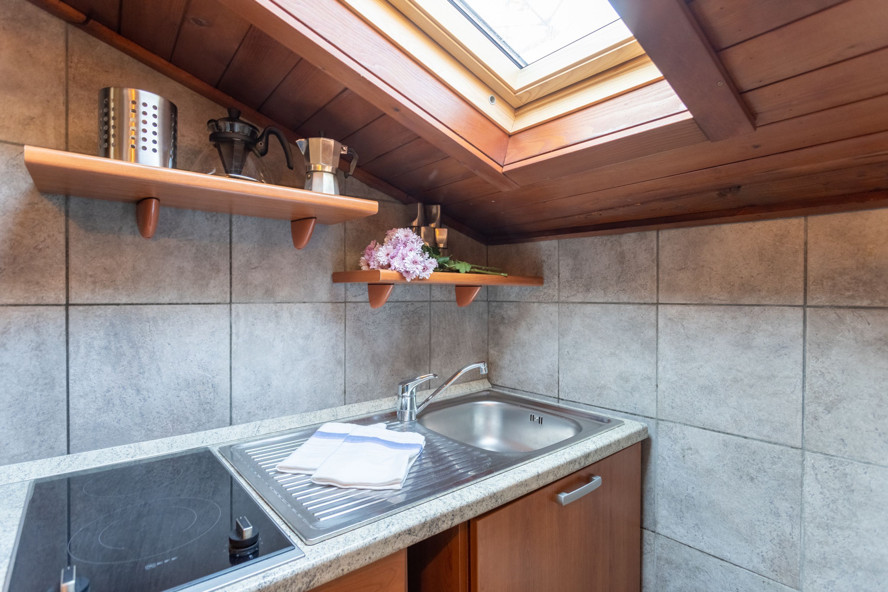 A kitchen with a built-in stove, a sink, wooden shelves, and a skylight.