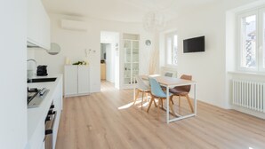 A modern kitchen with white cabinets, a built-in stove, and a dining area with a table and chairs. - Mezzegra Apartments in Tremezzo (Tremezzina)