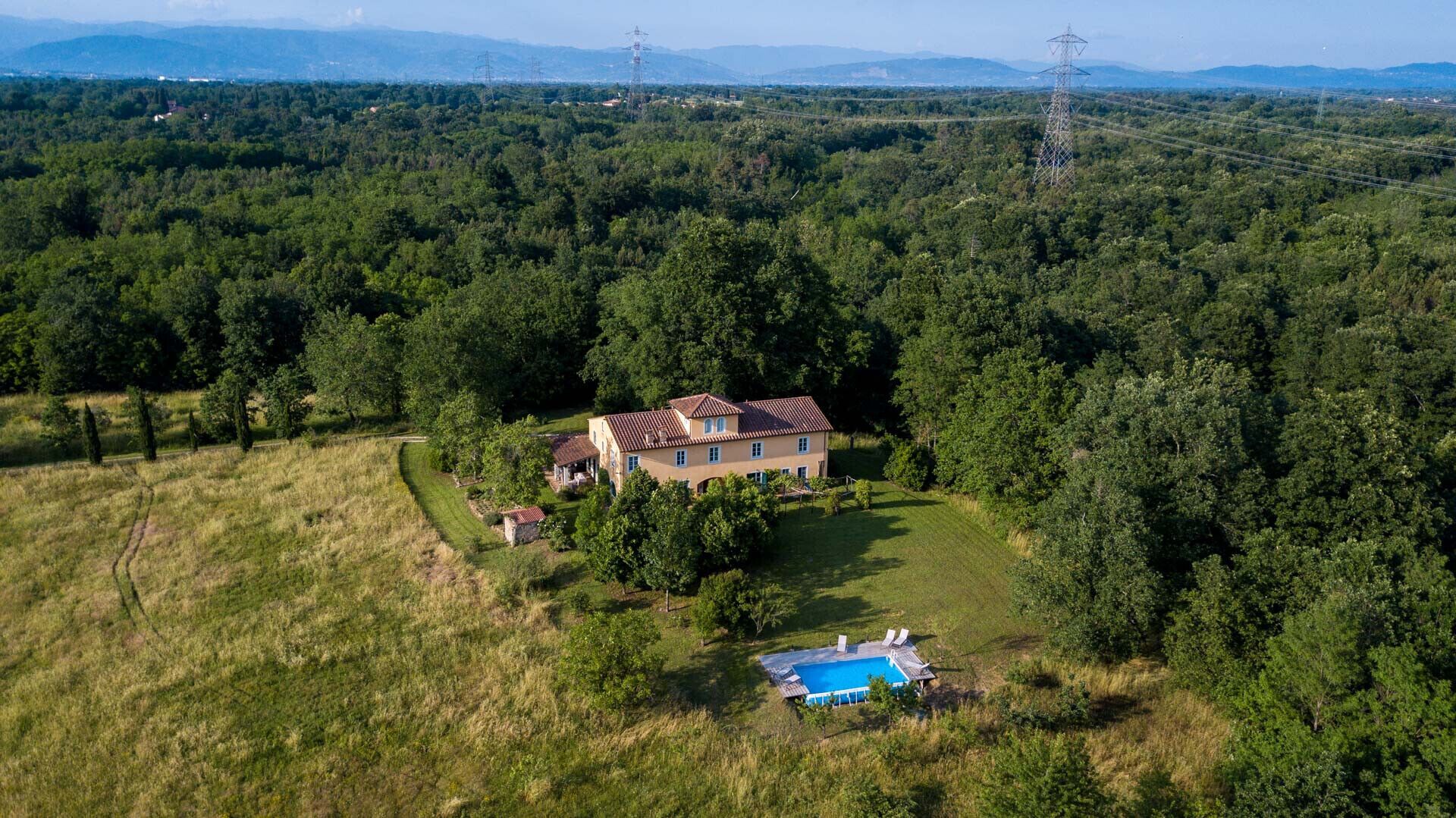 A large house with a swimming pool surrounded by dense forest.