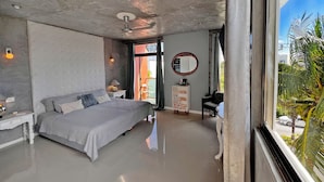 A modern bedroom with a large bed, a small bedside table, a nightstand, a dresser, a mirror, and a view of the outdoors.