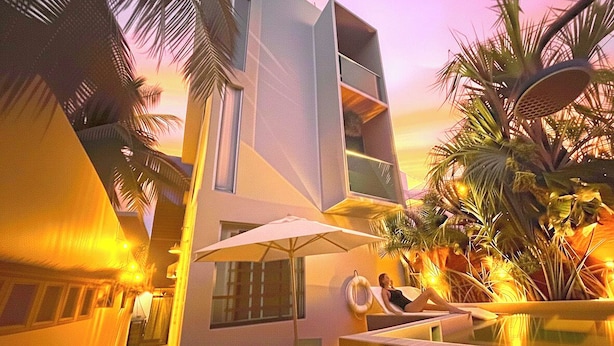 A modern building with a balcony, palm trees, and a pool area.