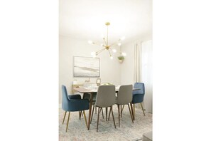 A dining area with a modern chandelier, a framed artwork on the wall, and a potted plant.