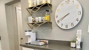 A kitchen area with a white cabinet, a clock, and shelves with coffee cups and a bottle. - 7 Mins to PHX Airport, Modern Boho, Sleeps 10 (Phoenix)