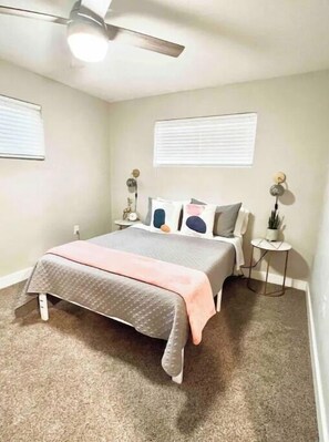 A bedroom with a bed, a ceiling fan, a nightstand, and a small table with a plant.
