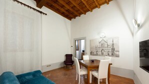 A dining area with a wooden table and chairs, a blue sofa, and a painting of a building on the wall. - Toscanella Apartment (Florence)