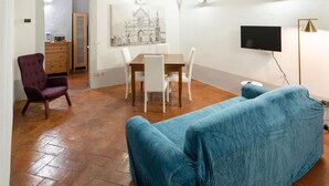 A room with a wooden ceiling, a dining table with chairs, a sofa, a TV, and a painting on the wall. - Toscanella Apartment (Florence)