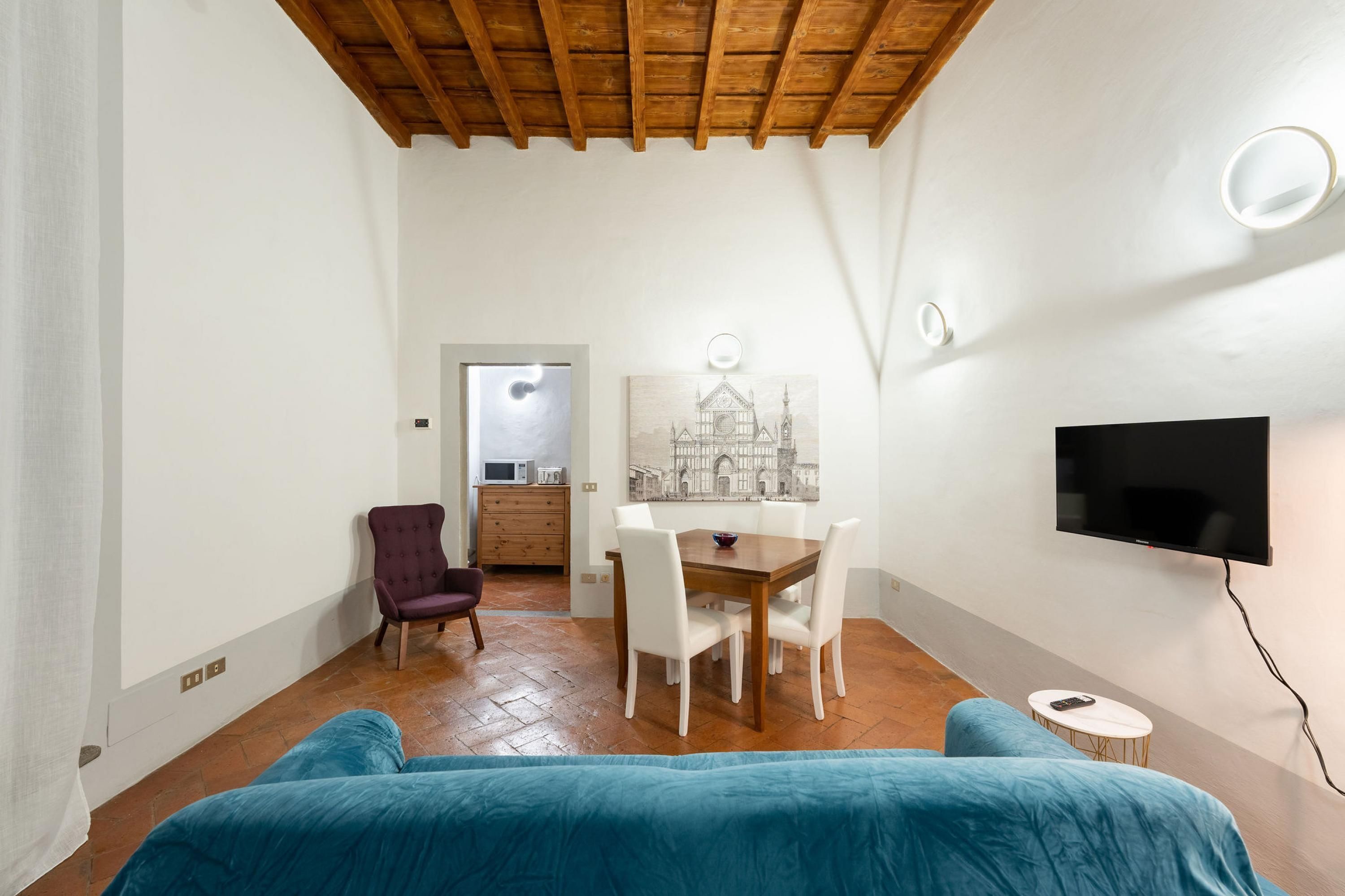 Une pièce avec un plafond en bois, une table à manger avec des chaises, un téléviseur fixé au mur et une petite table ronde avec une télécommande.