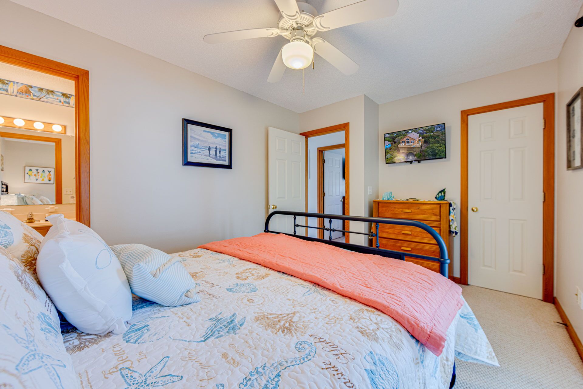 A bedroom with a bed, a dresser, a ceiling fan, and a door.