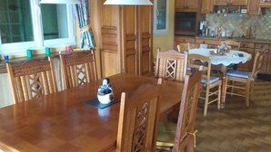 Een eetgedeelte met een houten tafel en stoelen, een decoratie op tafel, en een keuken op de achtergrond.