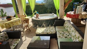 Een terras buiten met een jacuzzi, een zithoek en tafels.