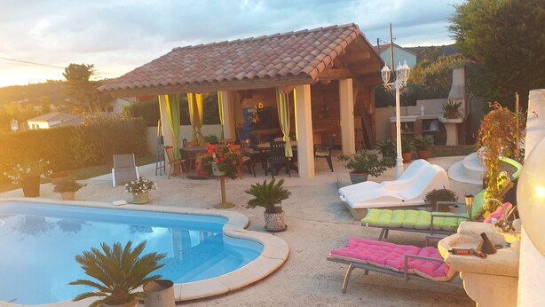 Een achtertuin met een zwembad, lounge stoelen, een pergola en een eethoek.