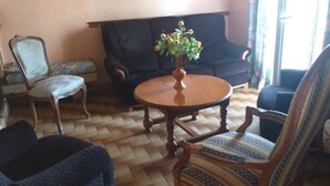 Een woonkamer met een ronde houten tafel, een bloemenvaas, een gestreept fauteuil en een donkere bank.