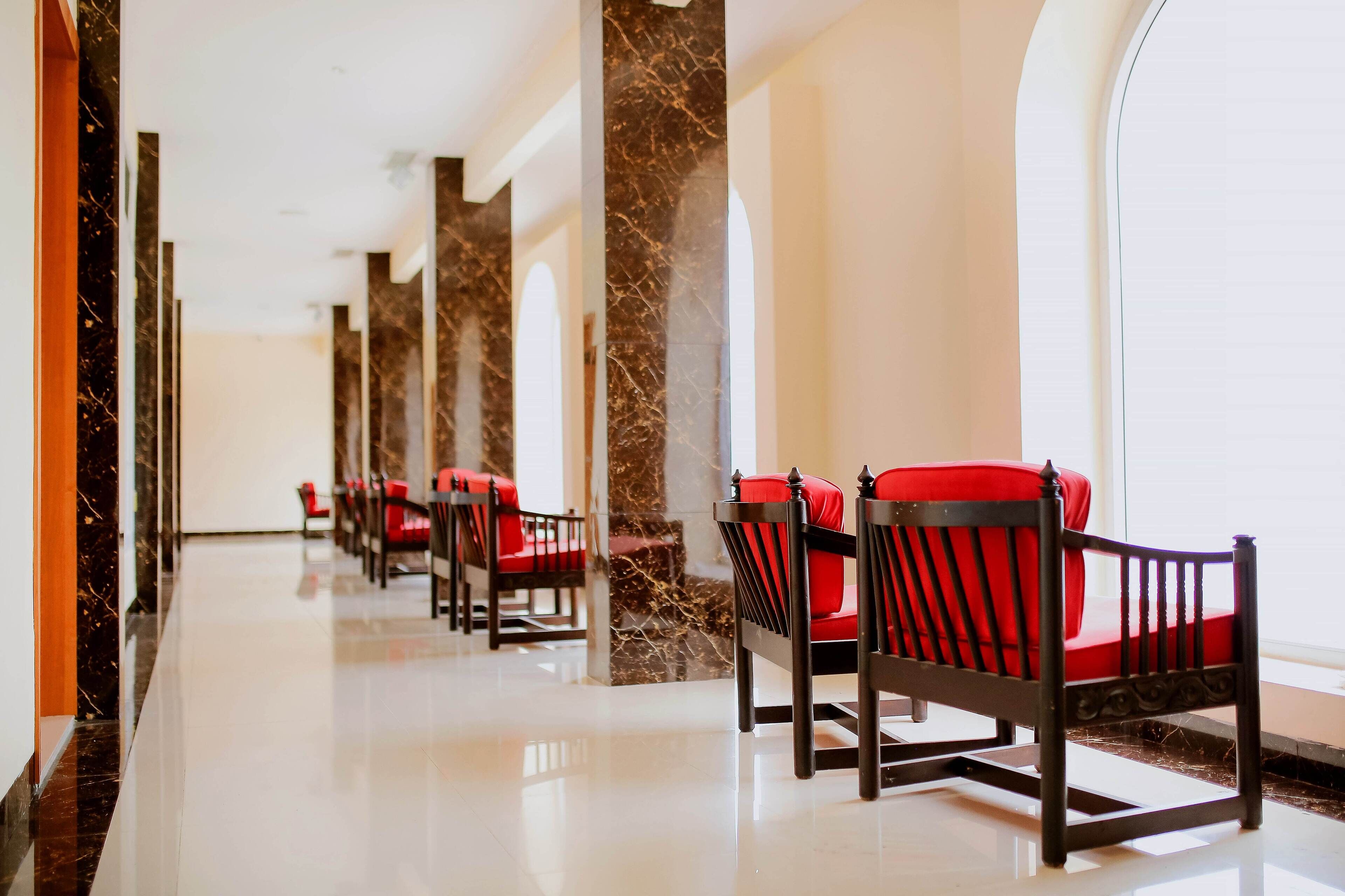 A hotel lobby with a marble column, red upholstered chairs, and a polished floor.