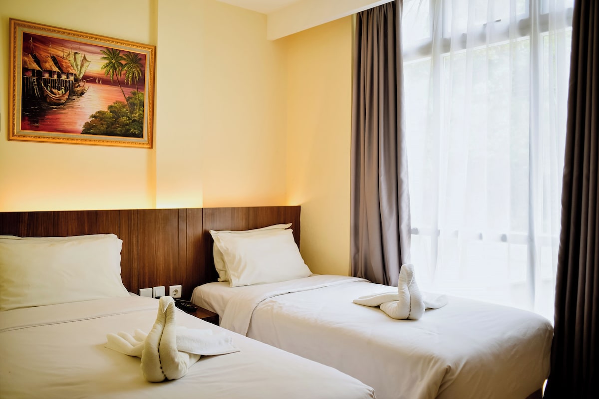Une chambre d’hôtel avec deux lits, un tableau au mur et une fenêtre avec des rideaux.
