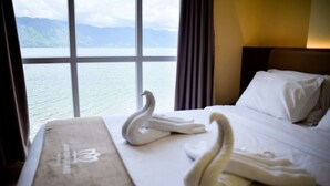 Una habitación de hotel con una cama, un ventanal con vistas a las montañas y al agua, y una toalla con forma de cisne sobre la cama.