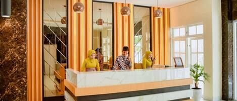 A hotel reception area with a marble counter, striped curtains, and a staircase in the background.
