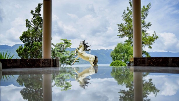 Una estatua de un caballo en un estanque que refleja el paisaje montañoso.