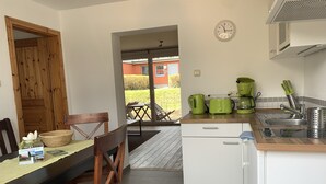 A compact kitchen with a dining area, featuring a wooden door, a dining table with chairs, a small refrigerator, and a coffee maker. - Waldhäuschen 6, Boltenhagen, 200m to the beach (Ostseebad Boltenhagen)