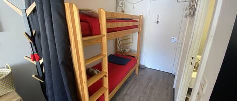 Une chambre avec un lit superposé en bois, une petite commode en bois et un rideau.