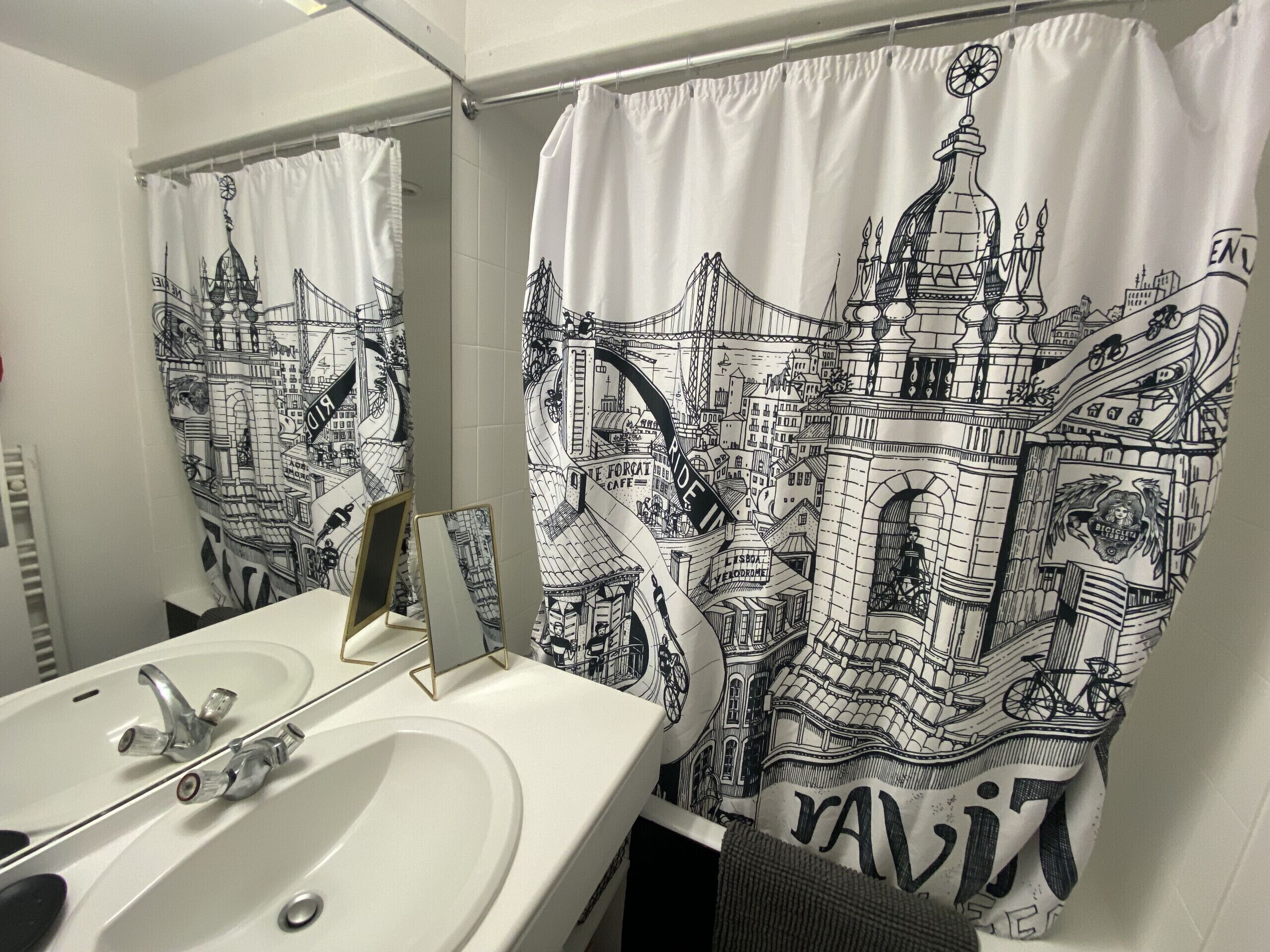 A bathroom with a white sink, a mirror, and a shower curtain featuring a cityscape design.