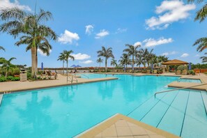 A swimming pool with multiple lanes, surrounded by palm trees and lounge chairs.