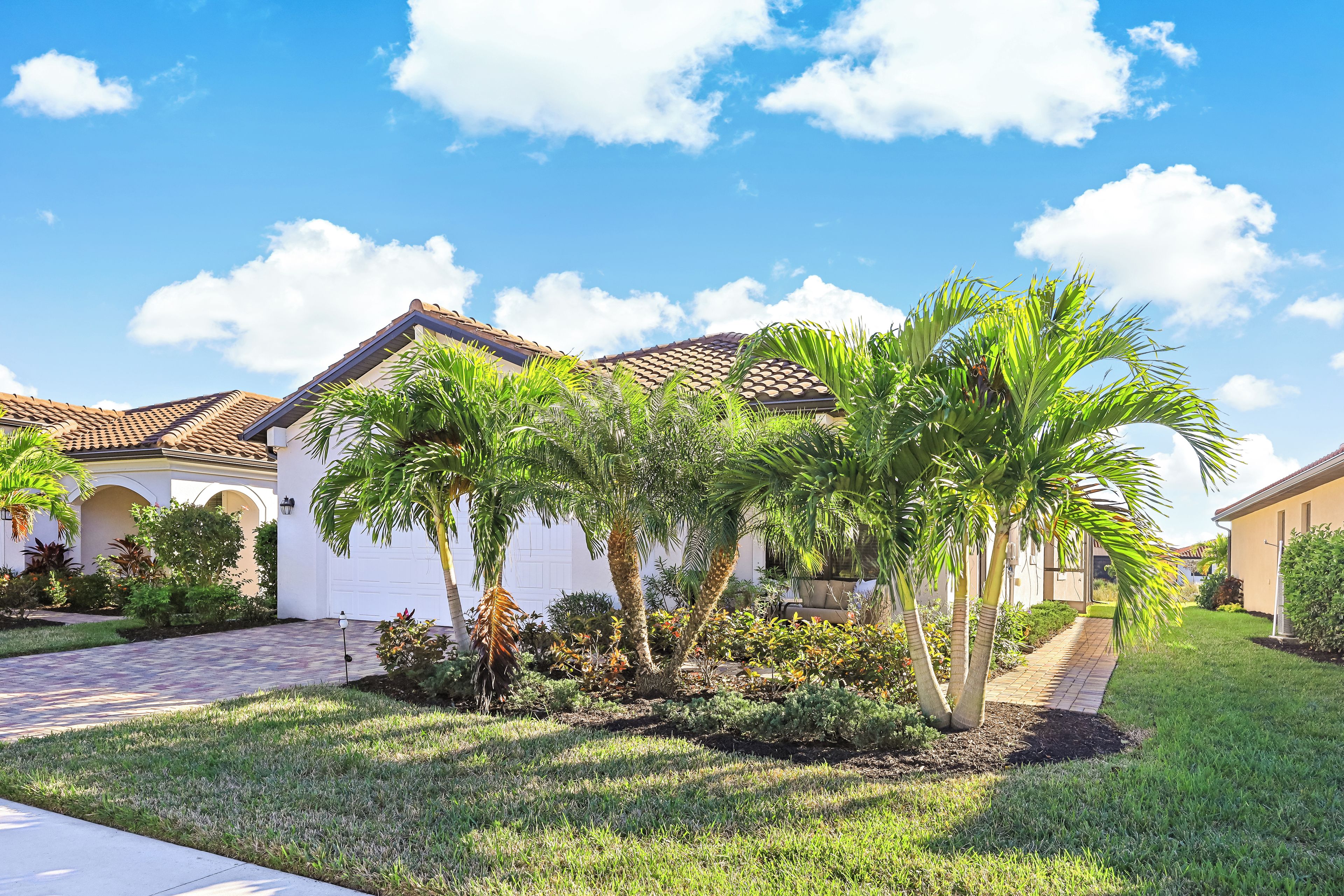 A residential area with a paved driveway leading to a white house with a tiled roof.
