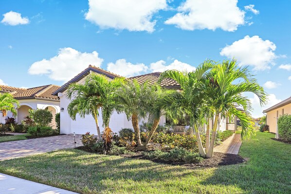 A residential area with a paved driveway leading to a white house with a tiled roof.